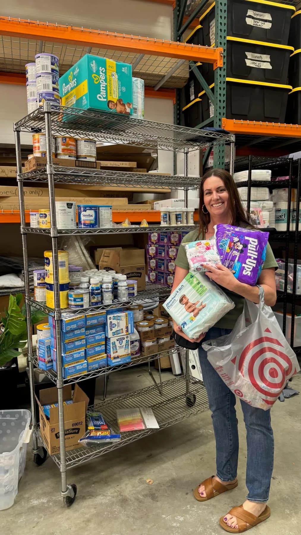 A woman holding packs of diapers in front of shelves stocked with formula and pantry goods